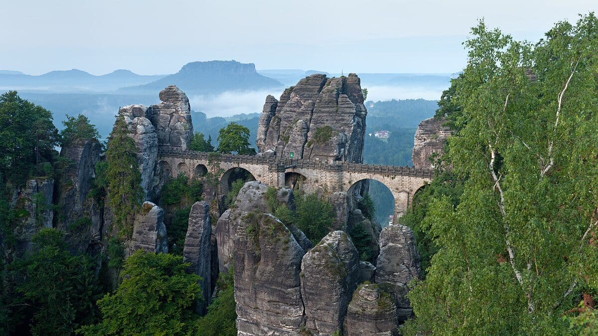 Basteibrücke zwischen Sandsteinfelsen im Morgennebel, im Hintergrund der Lilienstein