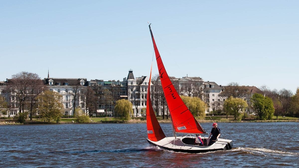 Segelboot mit rotem Segel auf der Außenalster vor den Villen am Ufer